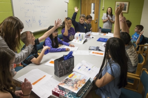 students sitting around table raising hands