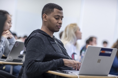 African American male student sitting at a desk looking at laptop