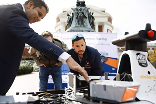 Three people bending down to look at a robot.