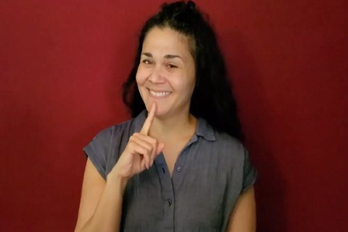 Woman standing in front of red background using sign language.
