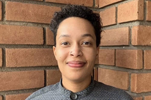 Kat Cosby wearing gray shirt standing in front of a brick wall