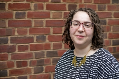 Sarah Orsak in front of brick wall looking at camera