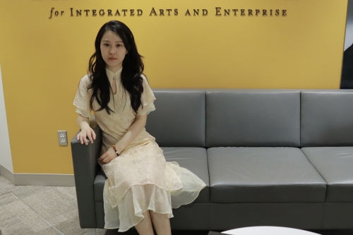 Yingchong Wang seated on gray sofa in front of yellow wall