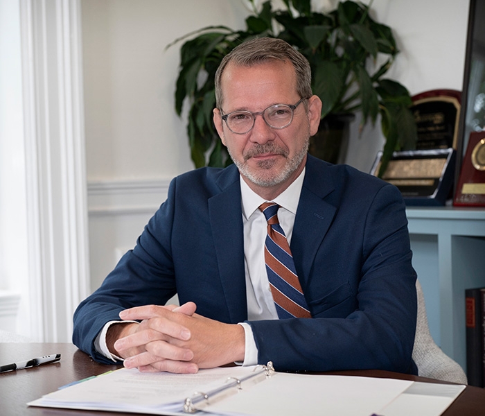 Provost Baucom seated at desk with hands clasped over notebook