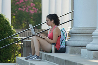 Female student sitting on steps with laptop on her lap